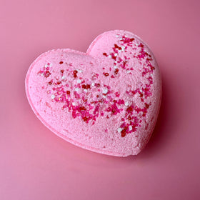 Heart-shaped pink bath bomb with glitter on a pink background