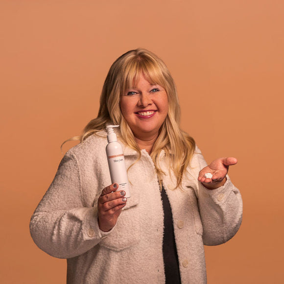 Woman holding a bottle and a small container against a brown background