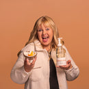 Woman holding a bowl of fruit and a bottle of skincare product against a brown background