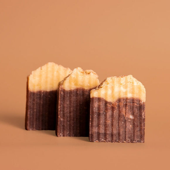 Three chocolate-covered looking bars of soap with a textured top sprinkled with cinnamon on a brown background