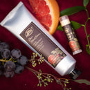 Hand cream and lip balm with grapefruit and grape elements on a red background