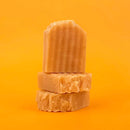 Three bars of brown soap stacked on an orange background