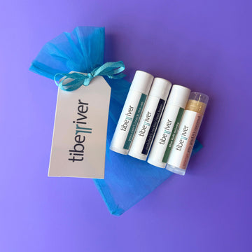 Tiberiver lip balm tubes with a blue gift bag on a purple background